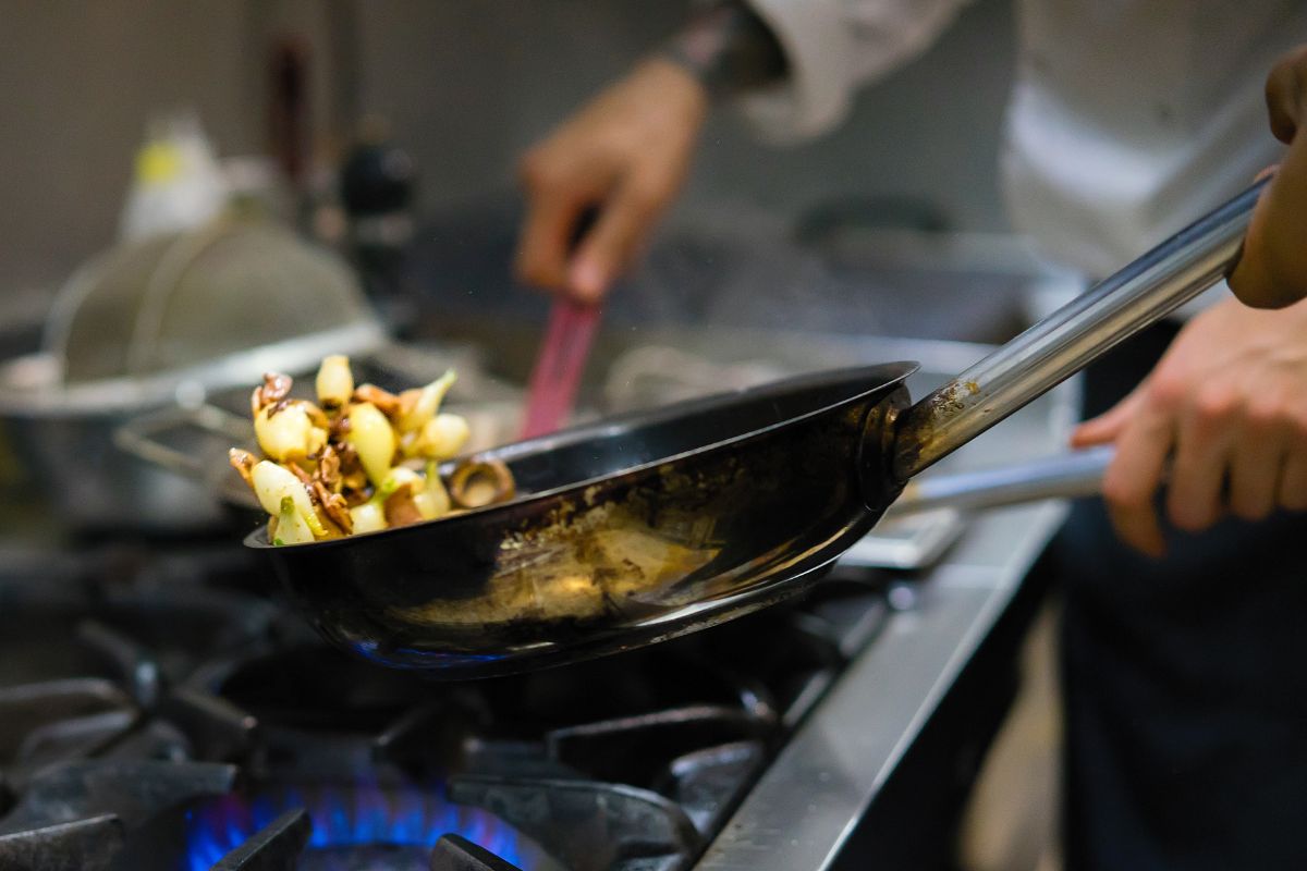 A chef cooking food in a pan over a gas hob