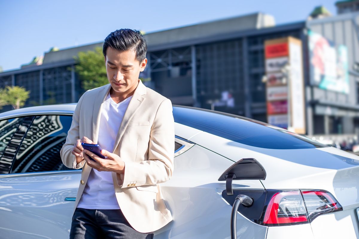 a man leaning against his EV plugged into a business EV charger