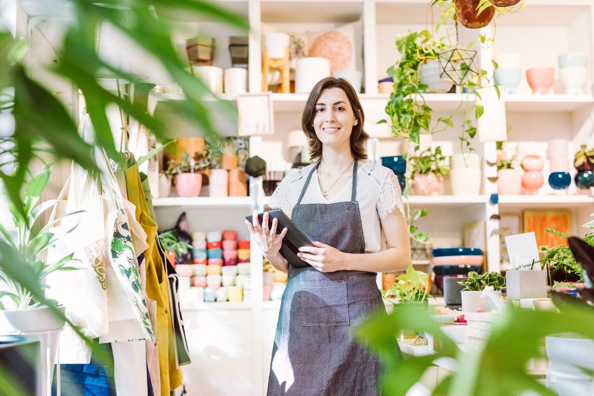 renewable energy for businesses - a business owner stands with an ipad in her shop. she wears and apron and is surrounded by plants