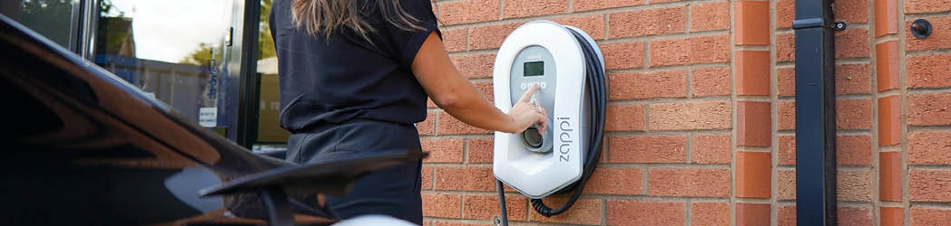 photo of a woman using an EV charger at her business outside an office building
