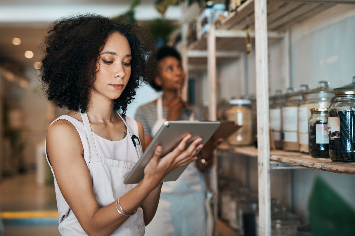 A woman in an apron researches alternative dispute resolution on her ipad whilst another woman in the background stocks shelves
