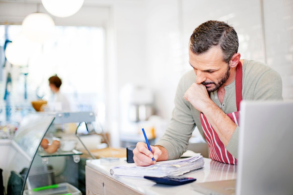 a man in a red apron writes don the details of his alternative dispute resolution on a notepad, with a deli environment in the background