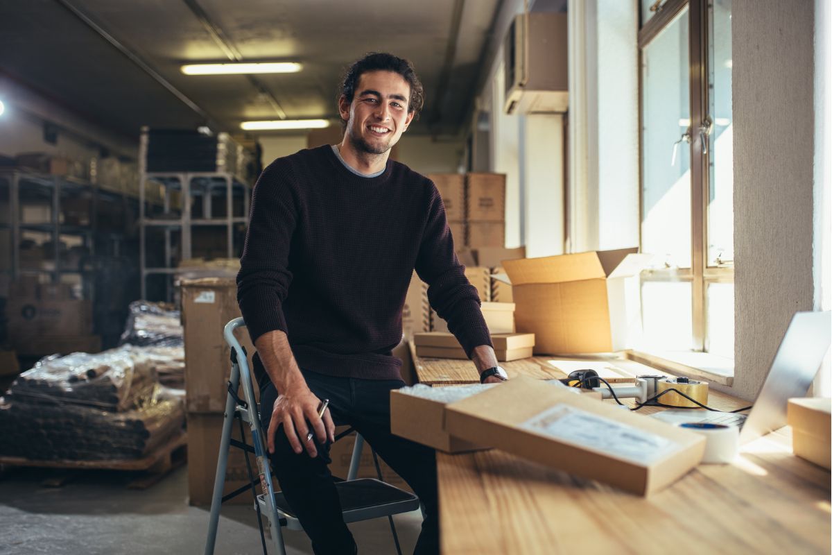A man sits on a high stool at a wooden desk in a workshop thinking about how long it takes to switch business energy supplier