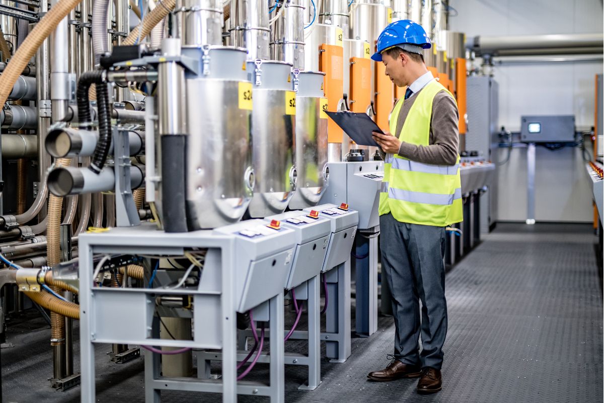 A man in a helmet and hi-vis vest inspects machinery in a factory