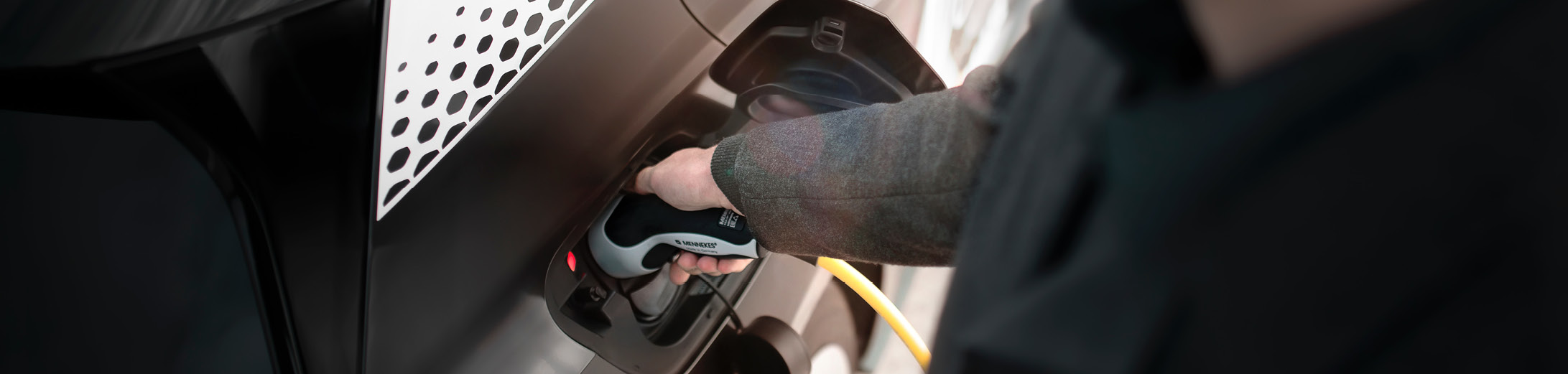 An image showing a closeup of someone plugging in an electric car to an EV charger. The car is black with a sporty check detail sticker.