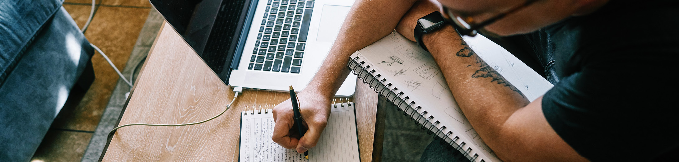 Someone writing up a social media strategy for small business. There is a notepad and laptop in the background.