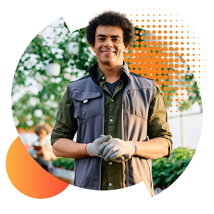Man wearing gardening gear and gloves standing in front of hanging baskets. He owns a large business - a garden centre.
