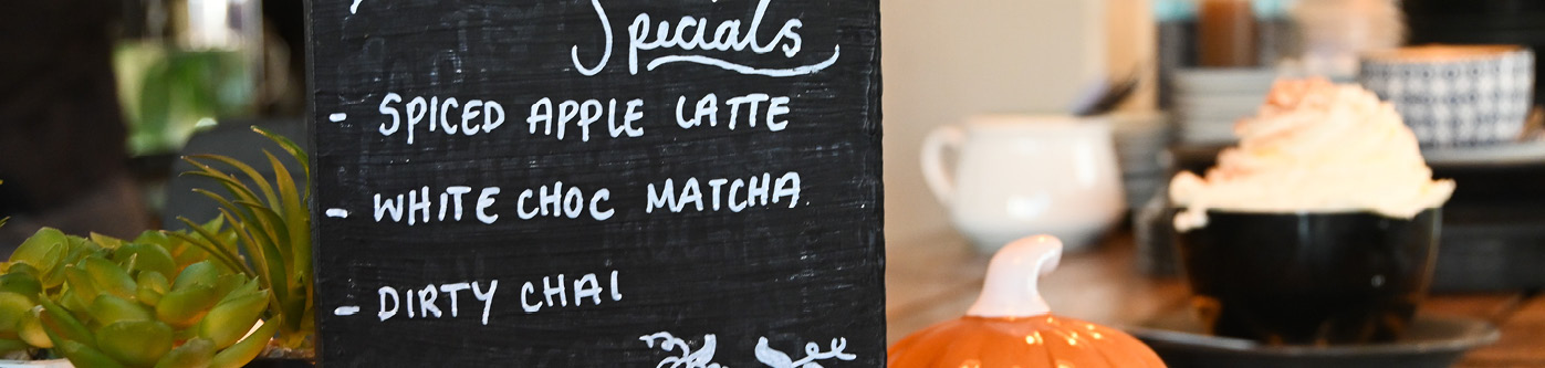 A halloween themed specials board in a cafe with pumpkins and hot drinks in the background