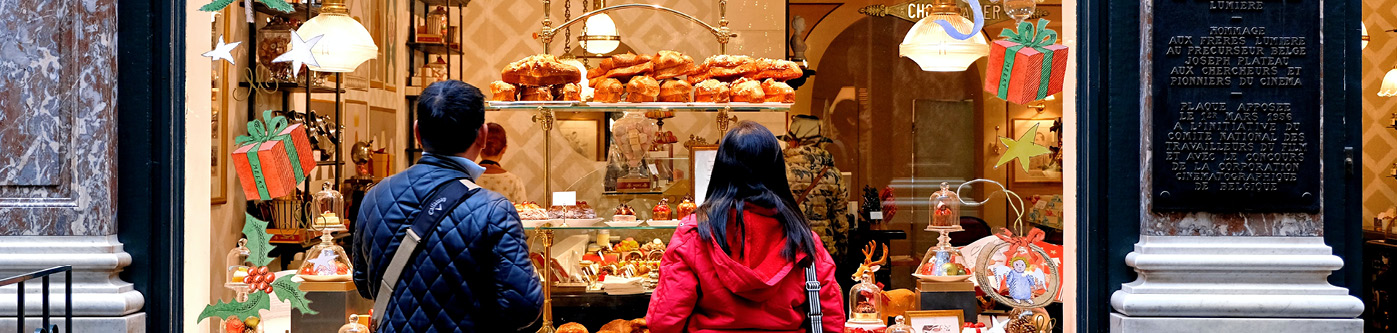 An image of a festive bakery shop window display, with hand painted graphics of presents and holly. Two people are looking into the window to get christmas business ideas.