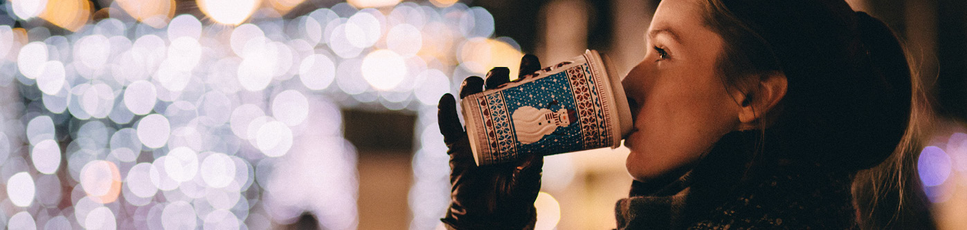 Christmas business ideas for customers - a woman in a winter hat and coat, sips a hot drink from a branded paper takeaway cup.