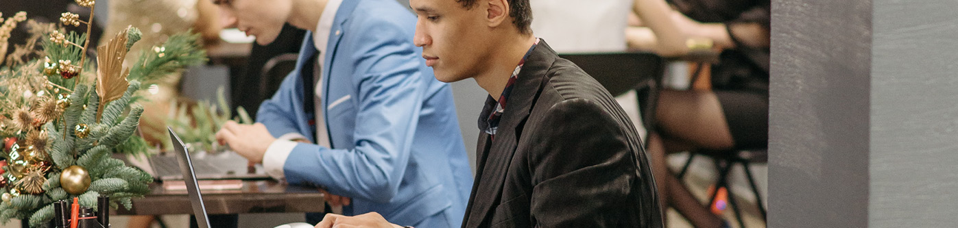 A male employee sat at his desk working on a computer with christmas decorations. It is quiet over christmas so he is preparing for the new year