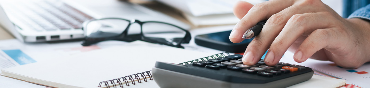Analyse your current energy usuage in the office. Image close up of a mans hand typing on a calculator.