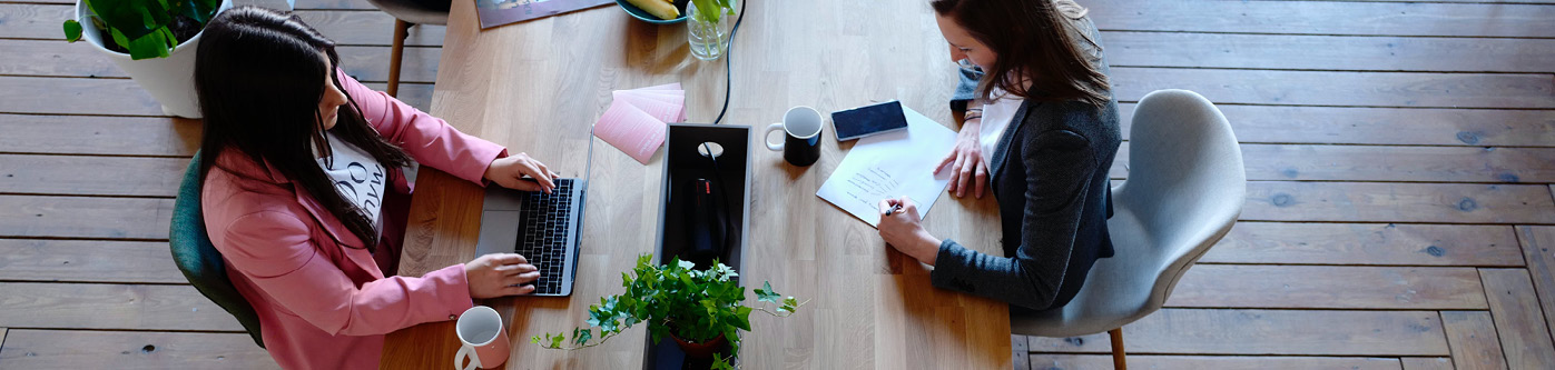 Two people sat across a long desk working on an email newsletter for their business
