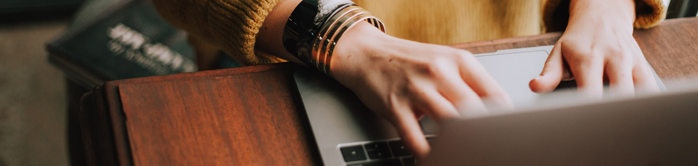 Hands typing on a laptop keyboard, sat on a wooden desk
