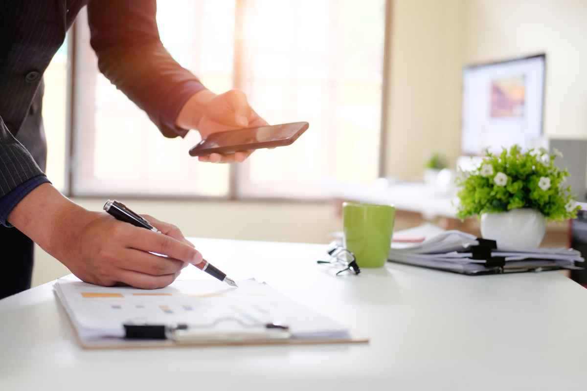 A close up, cropped in image of a business man checking his phone and making a new years business checklist