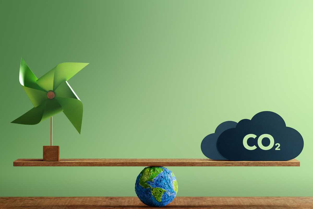 measuring business carbon footprint - illustrated by a green background and a desk, with a globe on top. atop the globe is a plank of wood, creating scales. on the left is a wind spinner and on the right is a cloud with 'CO2' written on.
