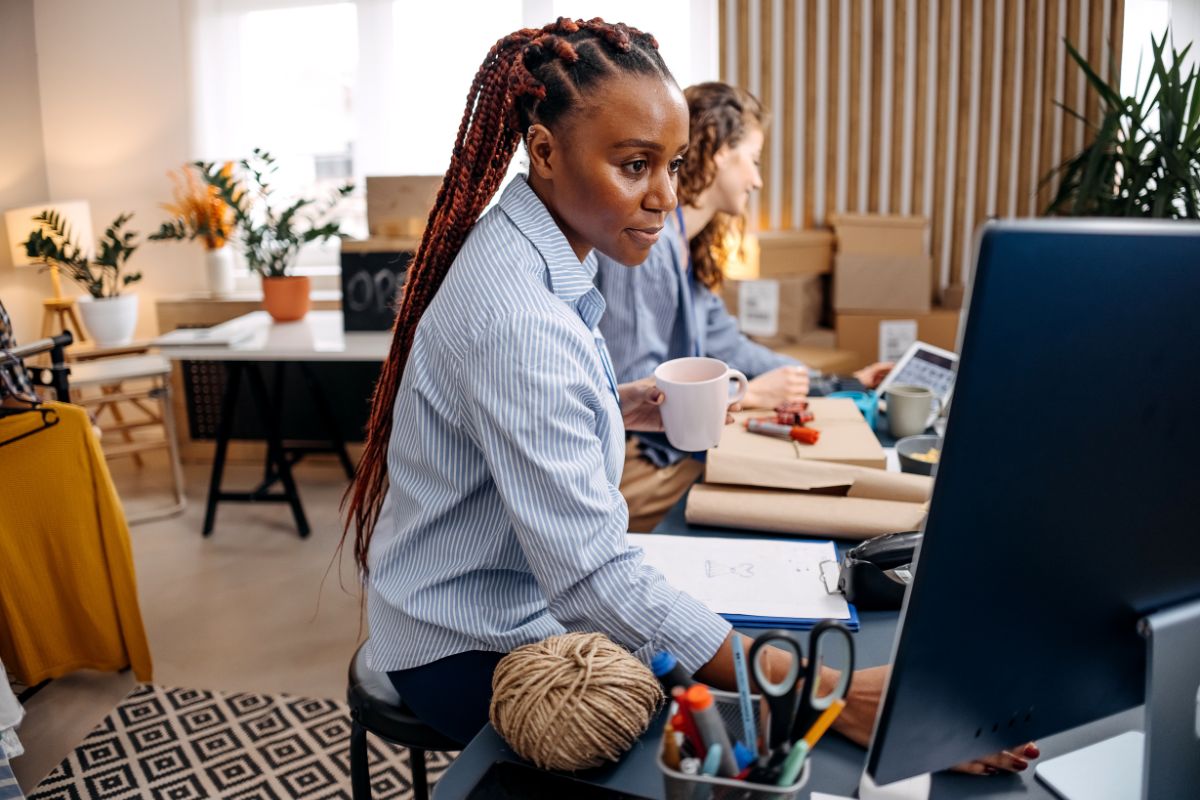 A woman in a blue shirt looking at a computer whilst drinking tea