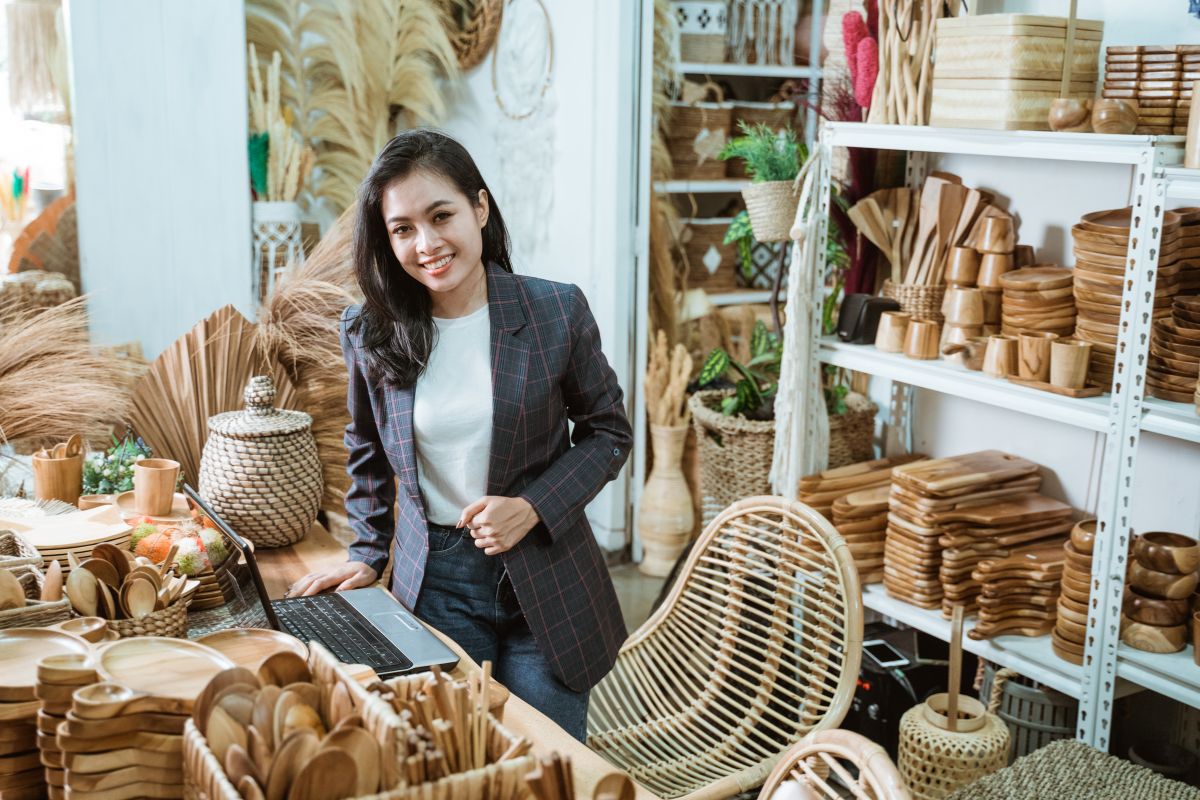 A female business owner in a dark suit surrounded by fully stocked shelves of wooden kitchen equipment