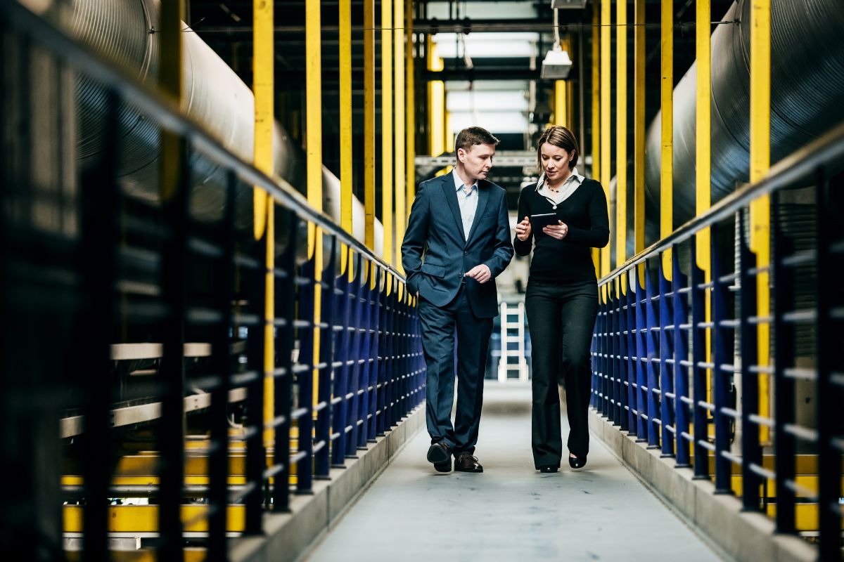 two colleagues, one male, one female, in business suits walk down the aisles of a warehouse whilst discussing their business energy switch