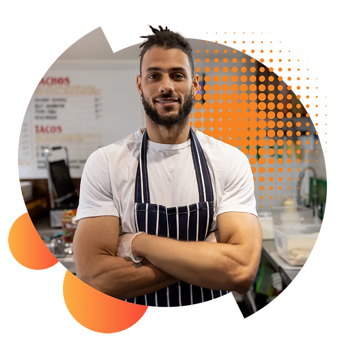 A man in a striped apron stands in his takeaway business with folded arms thinking about microbusiness energy solutions