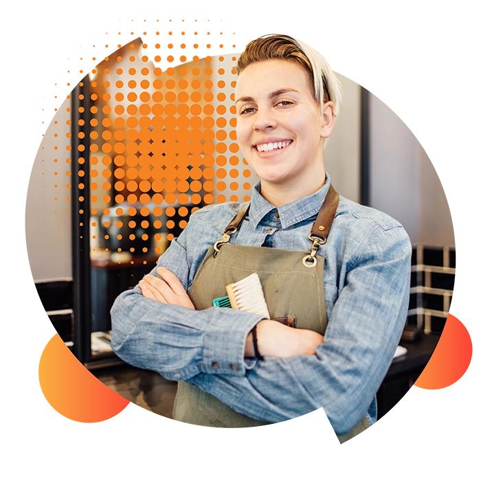 A female hairdresser with short blonde hair smiles at the camera with her arms folded after securing her microbusiness energy plan