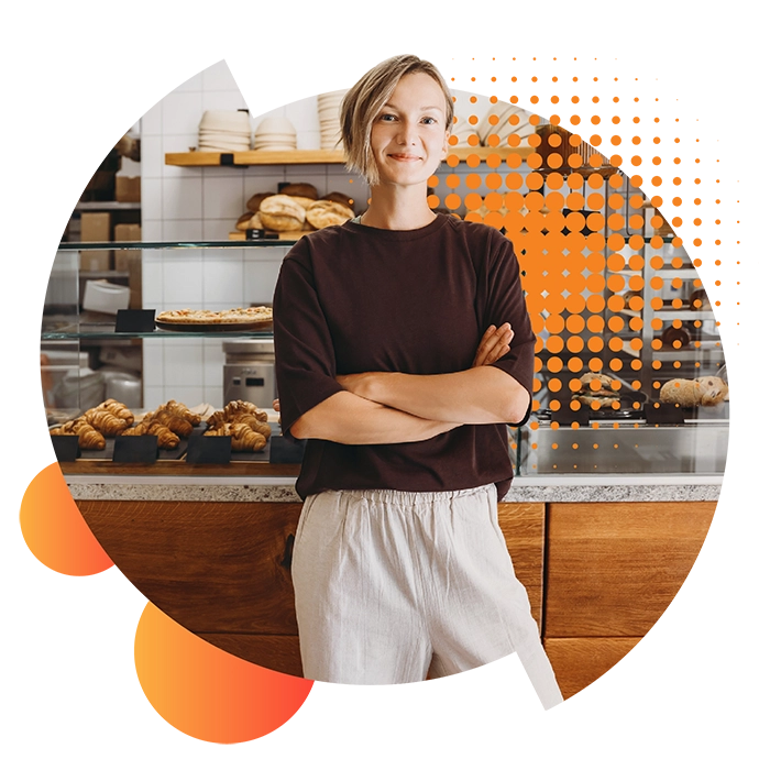 A confident woman leans against the counter of her bakery with arms folded thinking about her small business energy